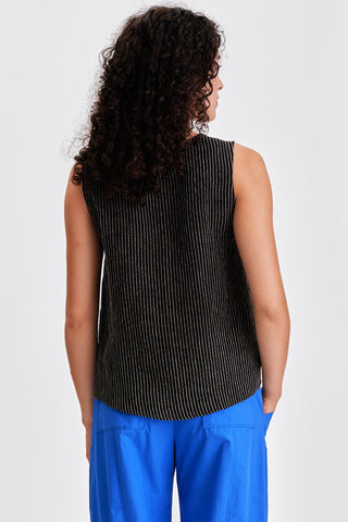 Back view of woman wearing a black striped tank top and blue pants in front of a white background