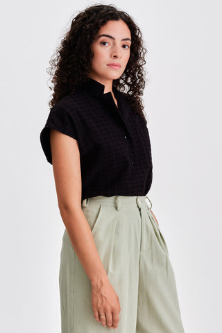 Woman wearing black button up shirt with light green pleated pants. 