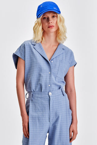 Woman wearing cobalt blue baseball cap and matching periwinkle blue button up shirt and pleated pants. 