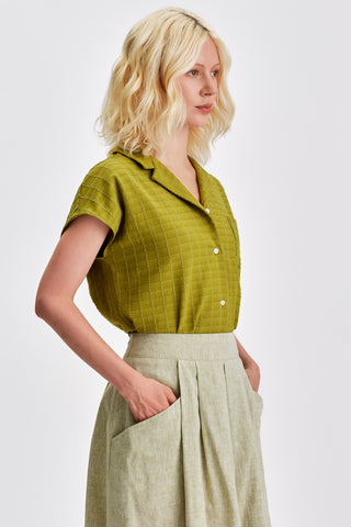 Woman wearing olive green button up shirt with light green skirt. 