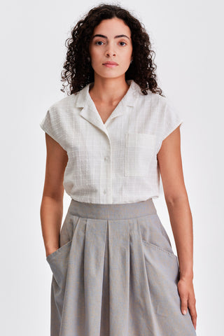 Woman wearing white button up shirt tucked into grey pleated skirt. 