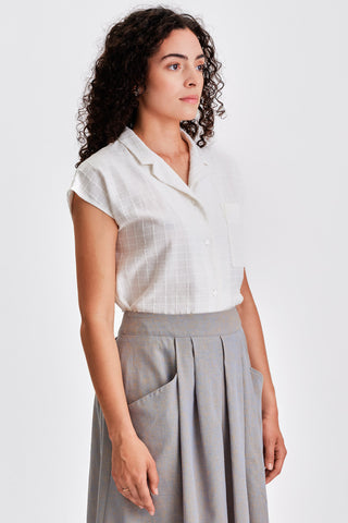 Side view of woman wearing white button up shirt tucked into grey pleated skirt. 