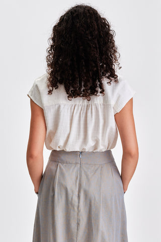 Back view of woman wearing white short sleeve blouse tucked into grey pleated skirt. 