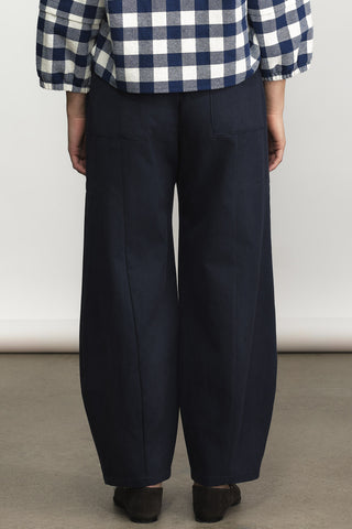 A person shown from the back wearing dark navy wide-leg trousers, a navy and white gingham shirt, and dark shoes, standing against a plain light gray wall.