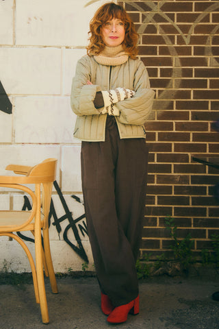 Designer Jennifer Glasgow in front of brick wall wearing quilted RAINS jacket, Rifo balaclava and gloves, JGD Dorset pants and red boots. 