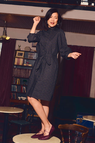 Woman dancing on table wearing black printed button up shirt dress and burgundy ballet flats. 
