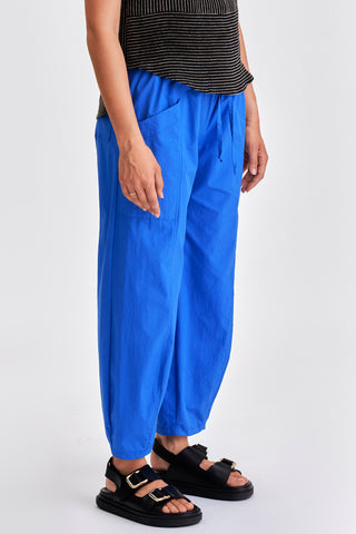 Side view of woman wearing black stripe tanktop, blue pants and black sandals. 