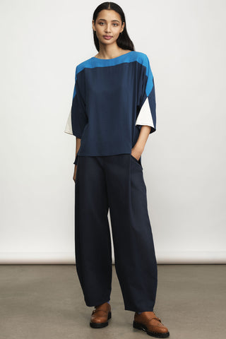 A model in studio wearing blue color-blocked top and navy barrel-cut trousers and brown brogue shoes. 