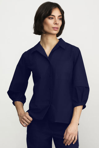 A woman modeling a navy button-up shirt with three-quarter sleeves, paired with black pants, against a light gray studio background.