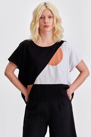 Woman in front of white background wearing black pants and black and white colour blocked oversized top. 