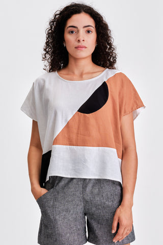 Woman in front of white background wearing grey shorts and white and orange colour blocked oversized top. 