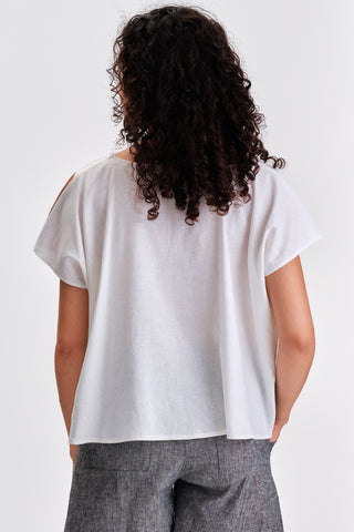 Back view of woman in front of white background wearing grey shorts and white and oversized top. 