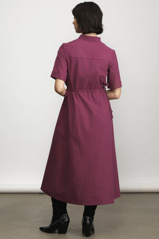 Back view of model in front of white wall wearing light burgundy midi length dress with button front and tie at waist. 