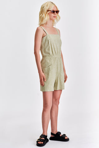 Woman wearing short light green romper with black sandals. 