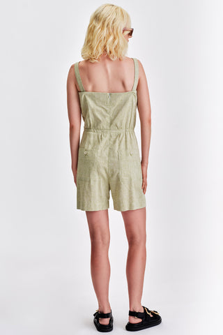 Back view of woman wearing short light green romper with black sandals. 