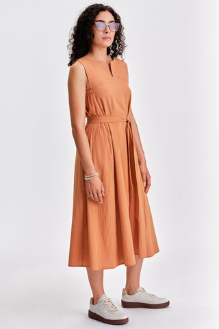 Woman wearing sunglasses, rust coloured  belted midi dress with white sneakers. 
