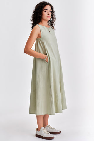 Woman with hands in her pockets, wearing light green sleeveless belted midi dress with white sneakers. 