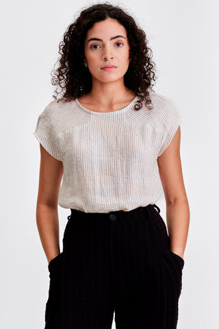 Woman in front of white background wearing white with black stripe cap sleeve top and black pants. 