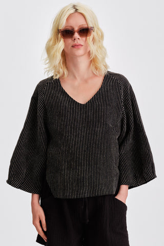 Woman in front of white background wearing sunglasses and black striped loose fitting v-neck blouse. 