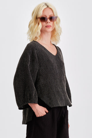 Woman in front of white background wearing sunglasses and black striped loose fitting v-neck blouse. 