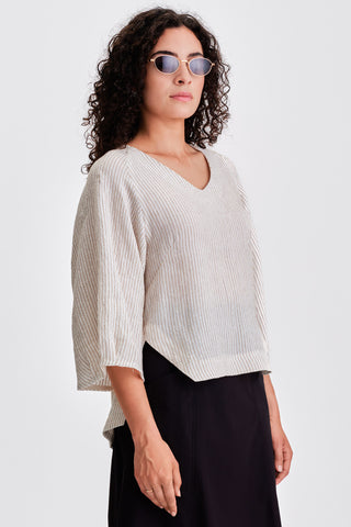 Woman in front of white background wearing white striped v-neck blouse with black skirt. 