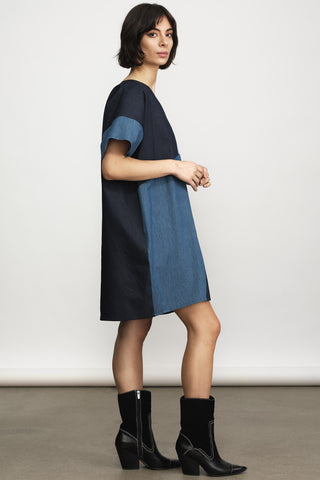 Side view of a woman wearing a loose, short-sleeve tunic dress with a two tone denim, paired with black ankle boots against a neutral studio background.