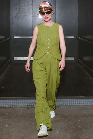 Jennifer exiting a freight elevator wearing green Vela vest and matching Cordelia pants. 
