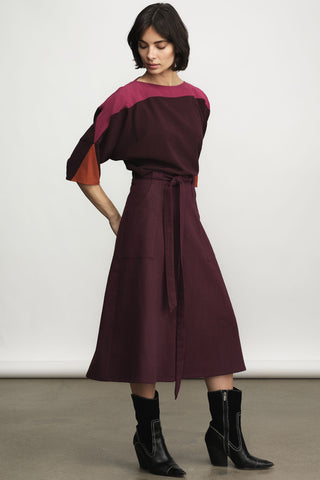 A model wearing a color-block blouse with a deep burgundy A-Line skirt, paired with black ankle boots, against a neutral studio background.