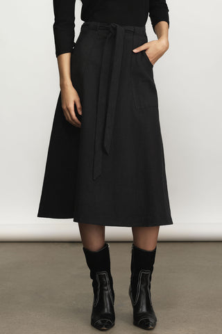 A model wearing a black midi a-line skirt with a tie waist, paired with black ankle boots, shown from the waist down against a neutral studio background.