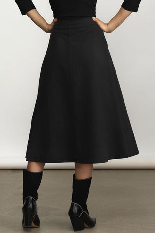 A black midi a-line skirt, shown on a model from the back. The model is wearing a black top and black knee-high socks with black block-heeled boots.