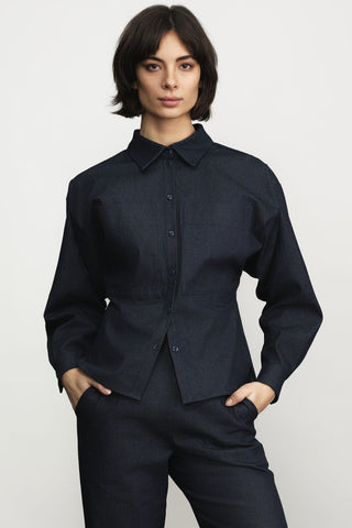 A woman modeling a dark navy denim long-sleeve button-up shirt and matching dark trousers against a light gray studio background.
