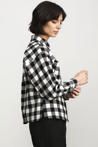 A woman wearing a black and white buffalo check plaid button-up shirt, shown from a side profile against a light gray studio background.