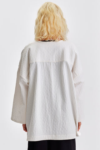 Back view of woman in front of white background wearing ivory kimono style jacket over black pants. 