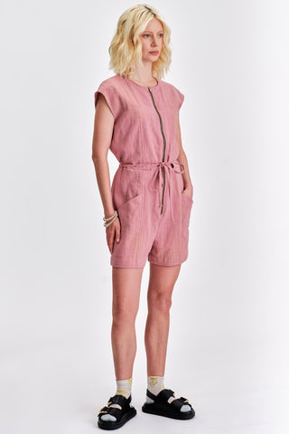 Woman in front of white background wearing pink short jumpsuit with black sandals. 