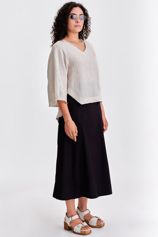 Woman in front of grey background wearing white stripe blouse and black mini length skirt.