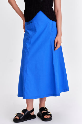 Woman in front of white background wearing bright blue midi length skirt with black sandals. 