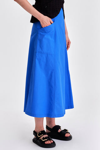 Woman in front of white background wearing bright blue midi length skirt with black sandals. 