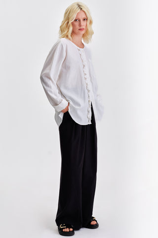 Woman in front of grey background wearing white blouse, black wide leg pants and black sandals. 