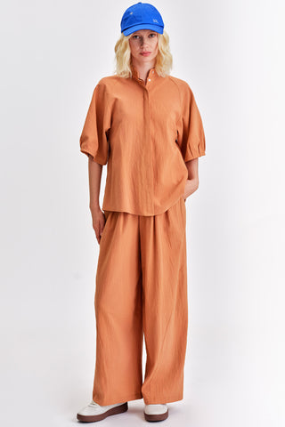 Woman wearing matching rust blouse and wide legt pants with blue cap and white sneakers. 