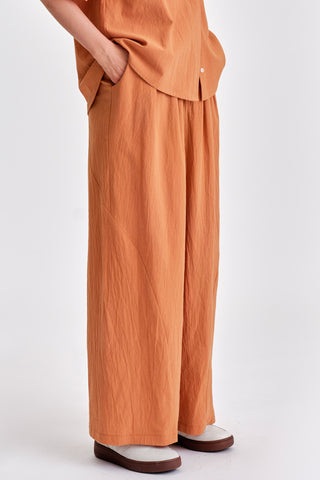 Woman wearing matching rust blouse and wide legt pants with white sneakers. 