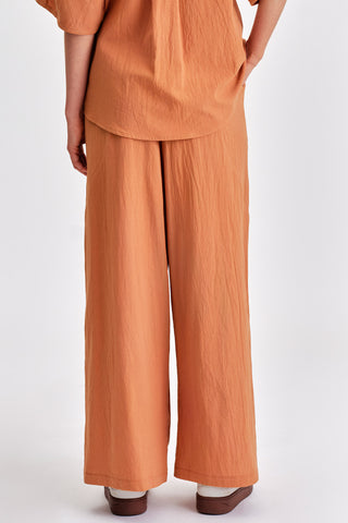 Back view of woman wearing matching rust blouse and wide legt pants with white sneakers. 