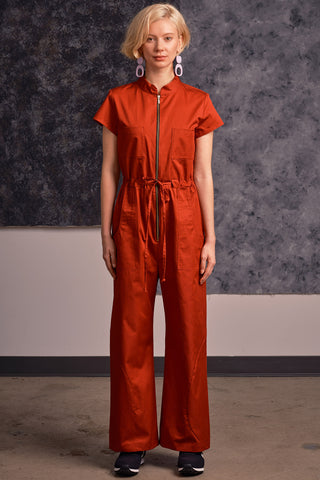 Model wearing brick red organic cotton zip up Anath jumpsuit by Jennifer Glasgow. 