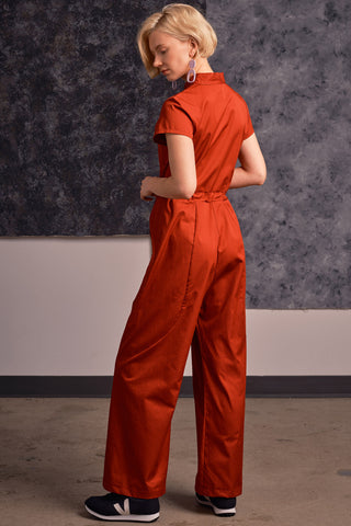 Back view of model wearing brick red organic cotton zip up Anath jumpsuit by Jennifer Glasgow. 