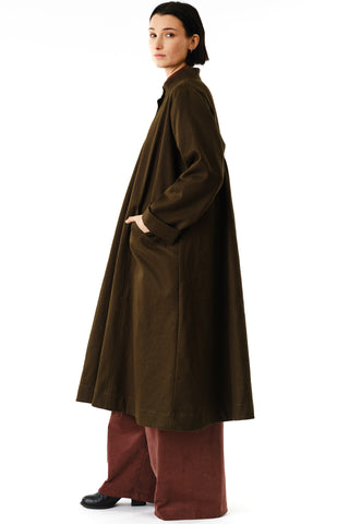 Side view of woman in front of white background wearing olive oversized Aterian swing coat by Jennifer Glasgow. 