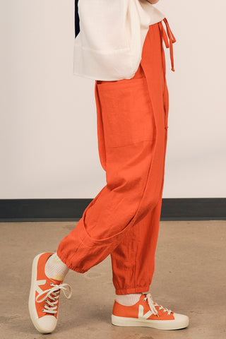 Side view of woman wearing coral red cotton track inspired Finnely Pants by Jennifer Glasgow. 