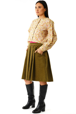 Woman against white background wearing floral button up top with olive green corduroy knee length Musica skirt by Jennifer Glasgow and black boots. 