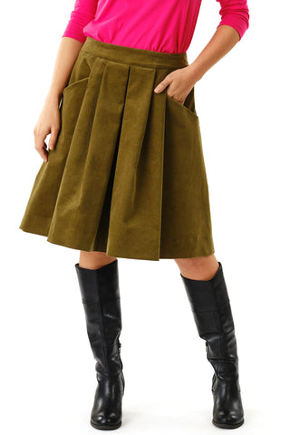 Close-up of woman against white background wearing olive green corduroy knee length Musica skirt by Jennifer Glasgow and black boots. 