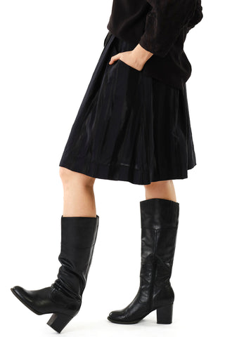Side view of woman in front of white background wearing black knee length Strenua skirt by Jennifer Glasgow and black boots.  