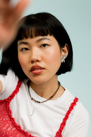 Woman in front of blue background wearing white t-shirt with lace red tank over top paired with bold silver flower shaped earrings. 