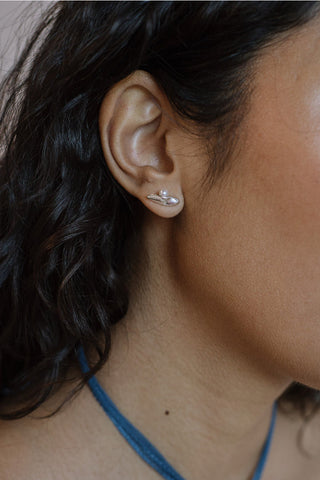 A close-up of a person's ear wearing a small silver & freshwater pearl stud earring.